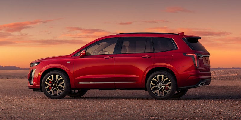 Side profile view of the 2025 Cadillac XT6 in red parked in a desert landscape at sunset