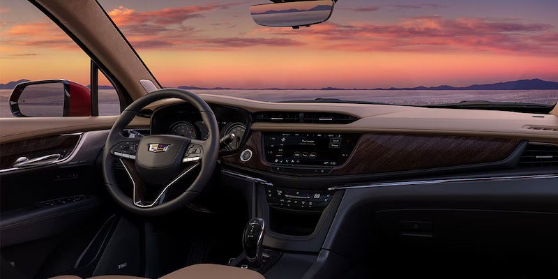 Wide interior shot of the 2025 Cadillac XT6 dashboard with wood trim and digital displays at sunset